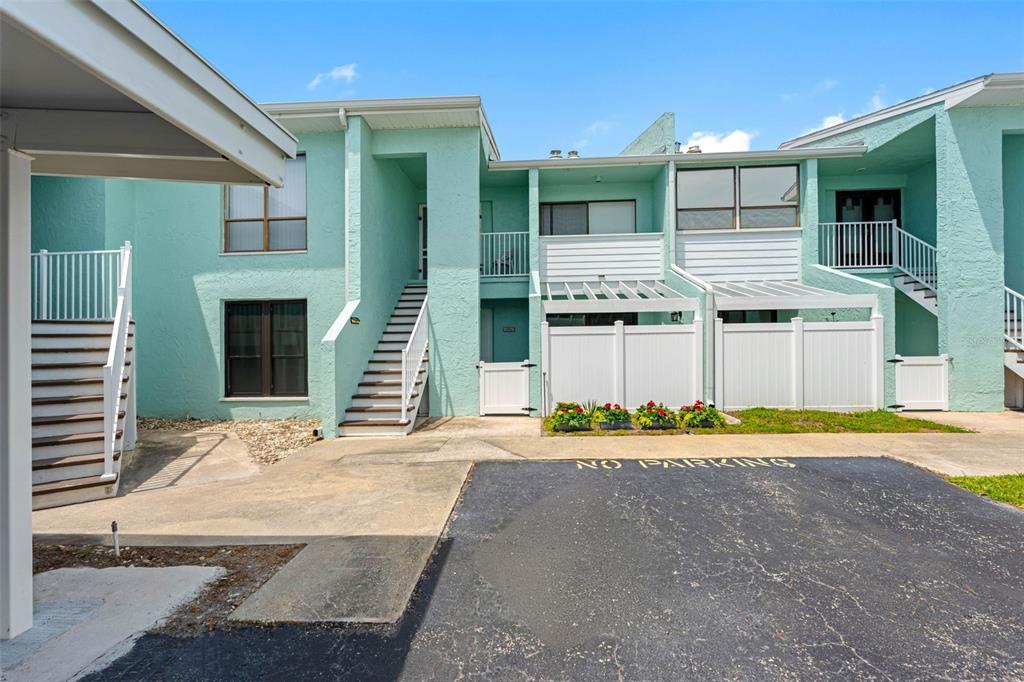 The exterior of a multi-story teal apartment building features white staircases and private fenced patios — 1 WINDRUSH BOULEVARD UNIT 101, INDIAN ROCKS BEACH, FL