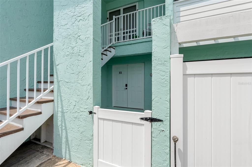 An exterior view of a teal building with a white staircase and a gated entrance — 1 WINDRUSH BOULEVARD UNIT 101, INDIAN ROCKS BEACH, FL