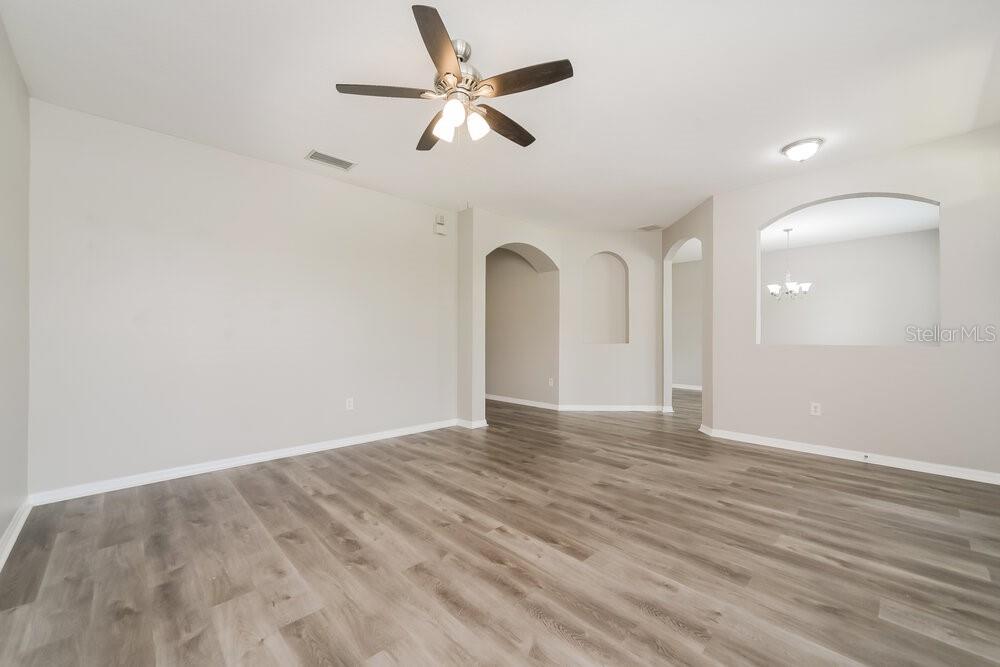 An empty room with light gray walls, wood-look flooring, and arched architectural openings — 3391 MARSHFIELD PRESERVE WAY, KISSIMMEE, FL