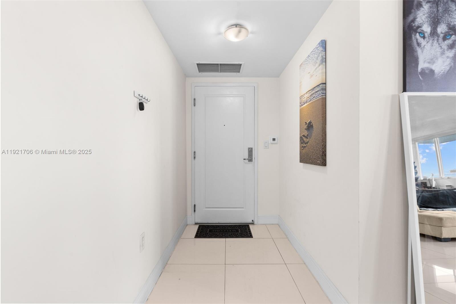 A white-walled entryway features a front door, tile flooring, and a wall-mounted beach painting — 1871 NW S River Dr # 1402, Miami FL 33125, MIAMI, FL