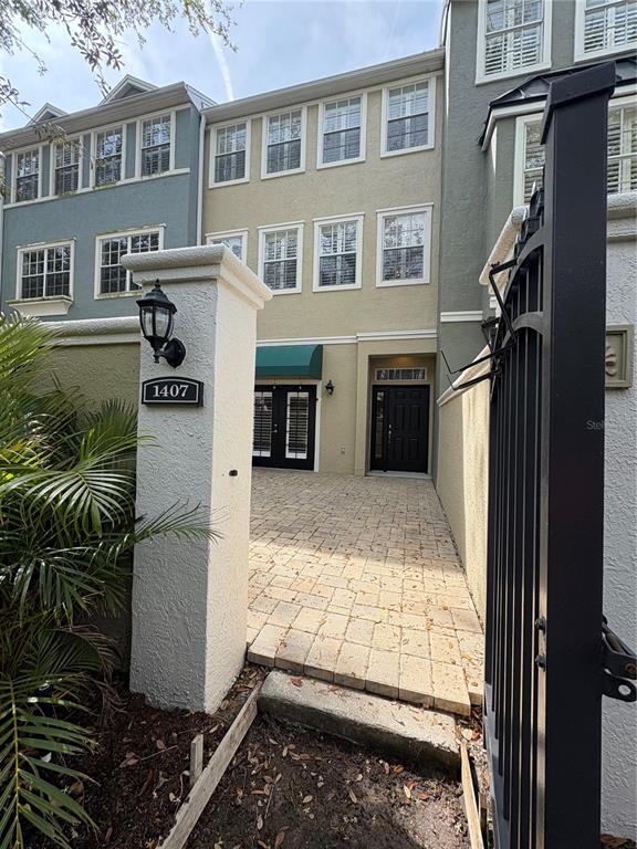 A paved courtyard leads to the front entrance of a three-story townhome with a gate — 1407 HARBOUR WALK ROAD, TAMPA, FL