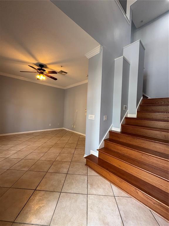 A room with light-colored tile flooring, a ceiling fan, and wooden stairs leading upward — 1407 HARBOUR WALK ROAD, TAMPA, FL