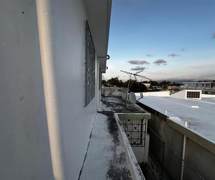 A narrow concrete balcony with a metal railing overlooks a neighboring rooftop and sky — 89 BLOCK 92 VILLA CAROLINA DEV. UNIT 11, CAROLINA, PR