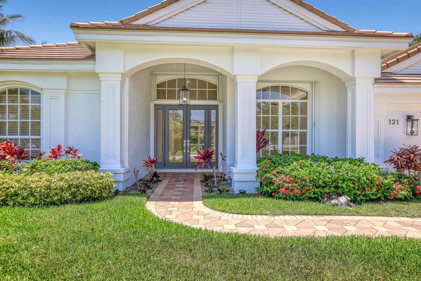 The exterior of a white house features a brick walkway leading to a double-door entrance — 121 Olympus Way, Jupiter FL 33477, JUPITER, FL