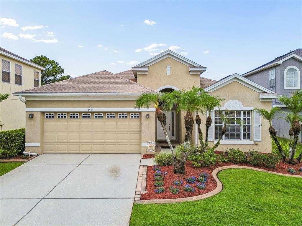 A single-story house with a beige stucco exterior, a two-car garage, and a landscaped yard — 3553 MORGANS BLUFF COURT, LAND O LAKES, FL