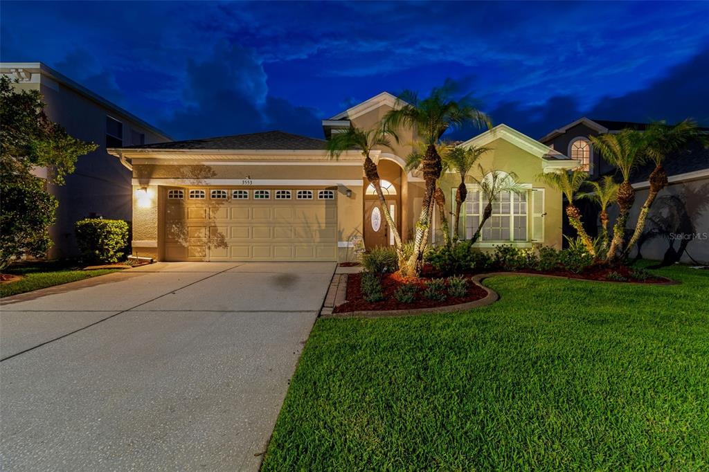 A single-story house with a beige exterior, a two-car garage, and palm trees at dusk — 3553 MORGANS BLUFF COURT, LAND O LAKES, FL