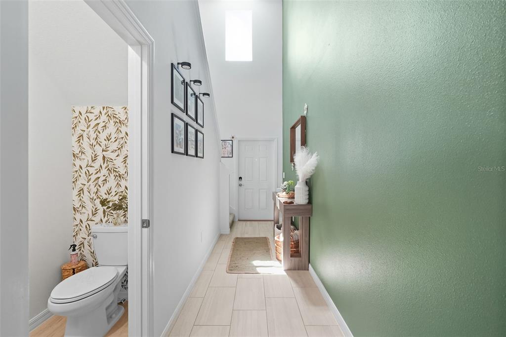 A hallway with light tile flooring, a green accent wall, and an adjacent half bathroom — 22289 NEBULA WAY, LAND O LAKES, FL