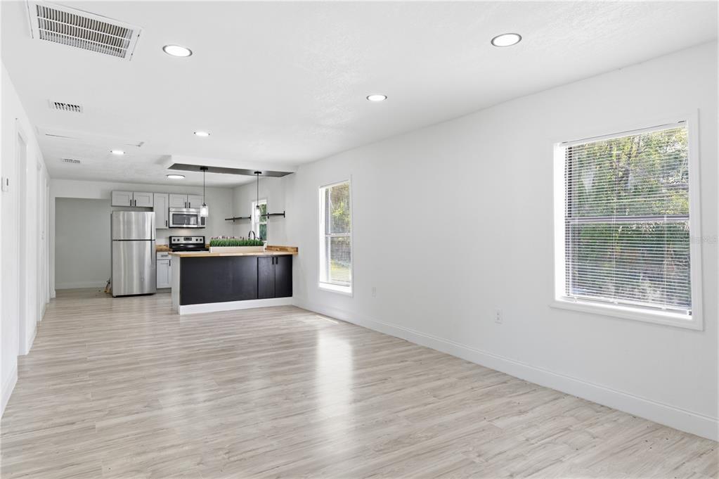A bright, open-concept living area features light wood-look flooring and a kitchen with dark cabinetry — 1104 E 8 TH STREET, SANFORD, FL