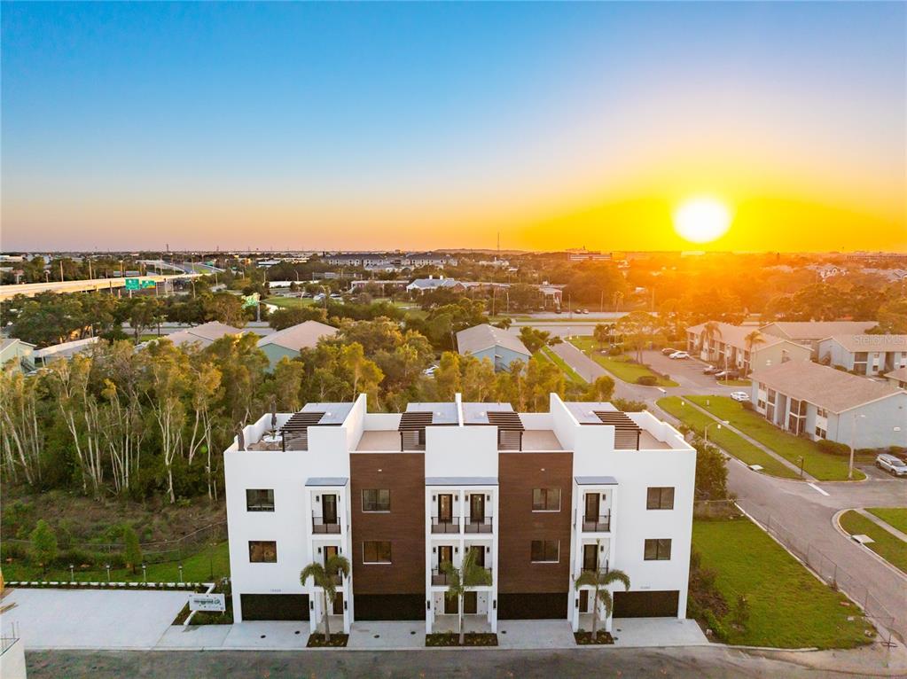 An aerial view shows a modern three-story townhouse complex at sunset with a wooded area — 10351 2ND STREET N, ST PETERSBURG, FL
