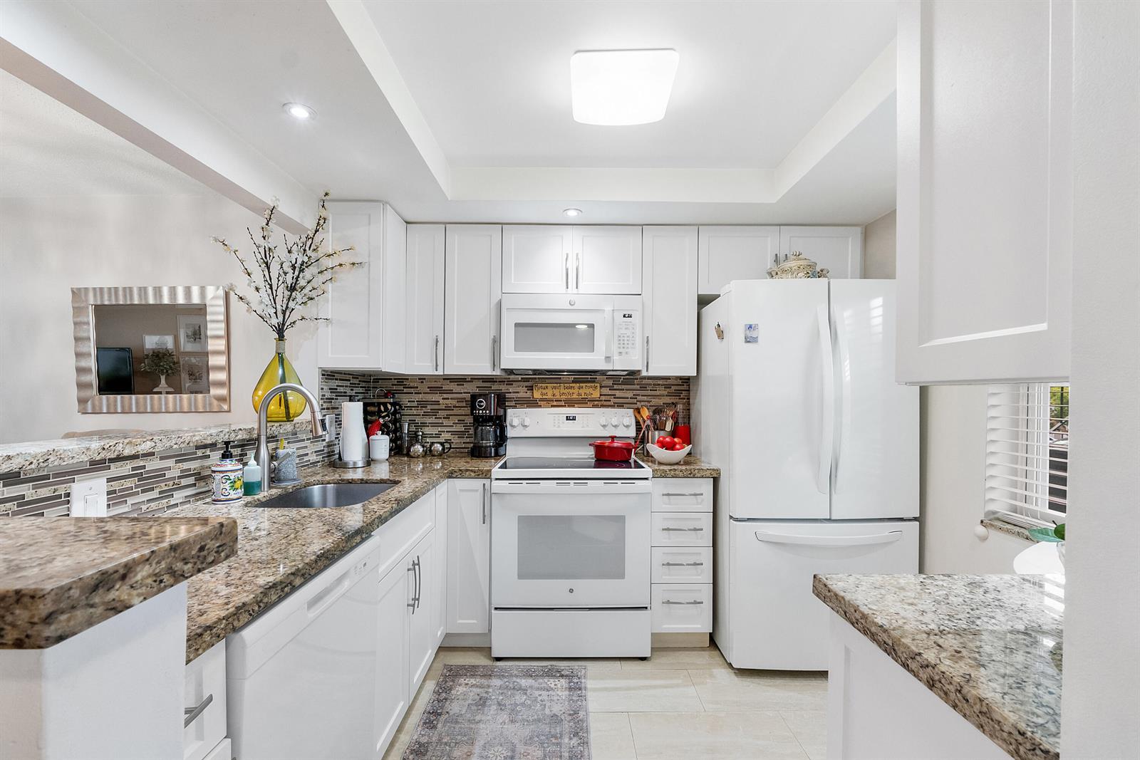 A kitchen features white cabinets, granite countertops, a stainless steel sink, and white appliances — 7837 Golf Circle Drive # 212, Margate FL 33063, MARGATE, FL