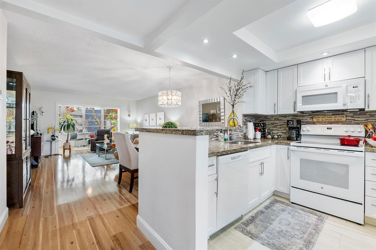 A kitchen with white cabinets and granite countertops opens into a living and dining area — 7837 Golf Circle Drive # 212, Margate FL 33063, MARGATE, FL