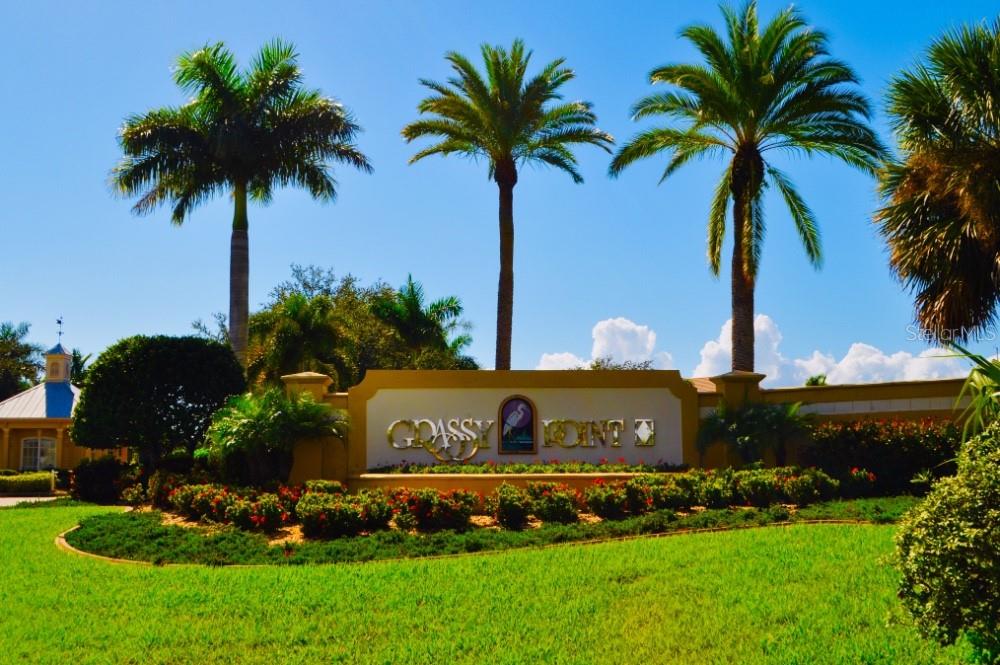 A sign for Grassy Point stands in a landscaped yard with palm trees under blue skies — 21421 HARBORSIDE BOULEVARD, PORT CHARLOTTE, FL