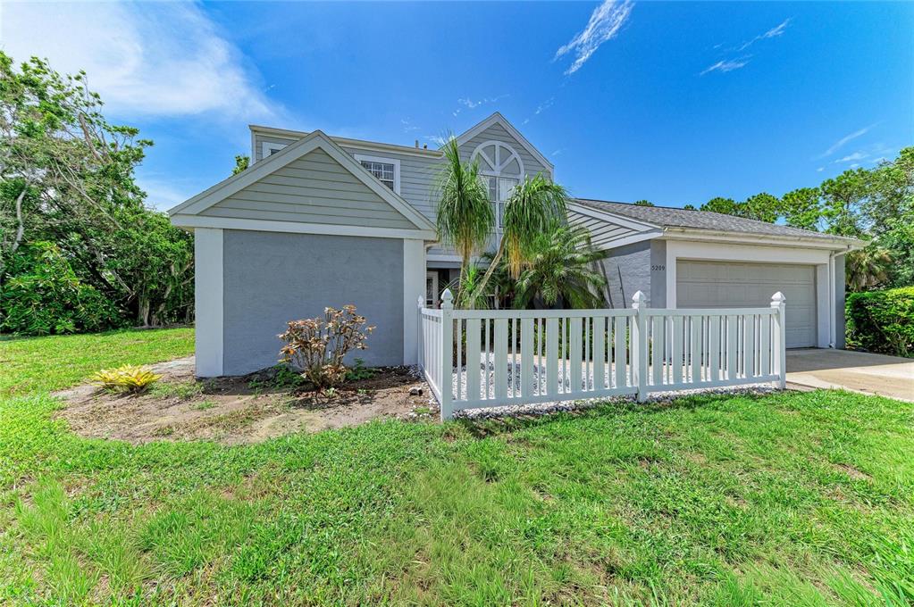 A two-story house with gray siding, a white picket fence, and a two-car garage — 5209 34TH STREET COURT W UNIT 261, BRADENTON, FL