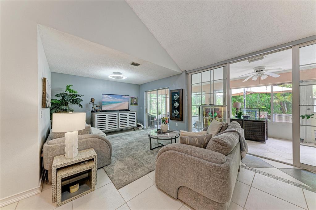 A living room features vaulted ceilings, tile flooring, gray furniture, and sliding glass doors to a patio — 5209 34TH STREET COURT W UNIT 261, BRADENTON, FL