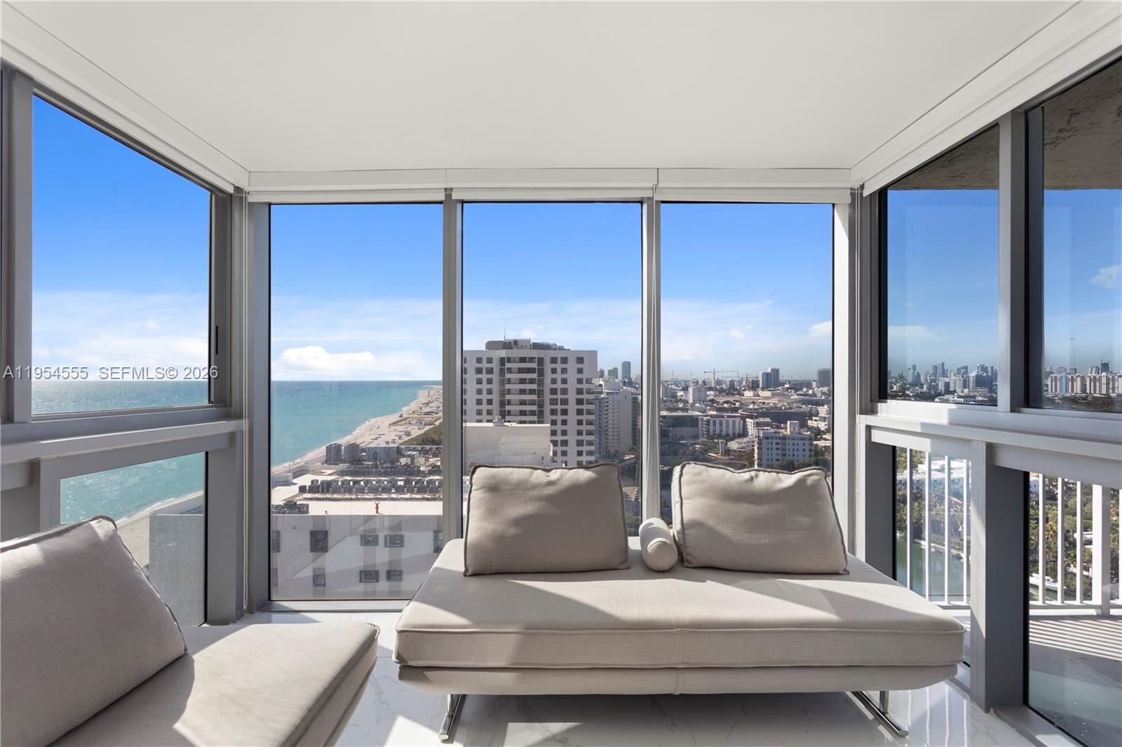 A sunroom with floor-to-ceiling windows overlooks the ocean and a city skyline — 2655 Collins Ave, Miami Beach FL 33140, MIAMI BEACH, FL