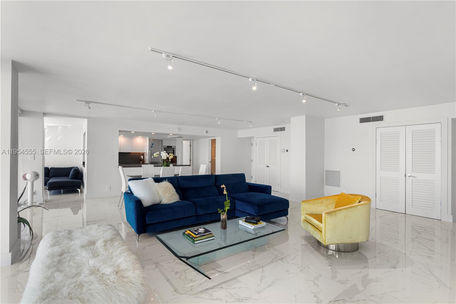 A living room features a blue sectional sofa, yellow armchair, glass coffee table, and marble floors — 2655 Collins Ave, Miami Beach FL 33140, MIAMI BEACH, FL