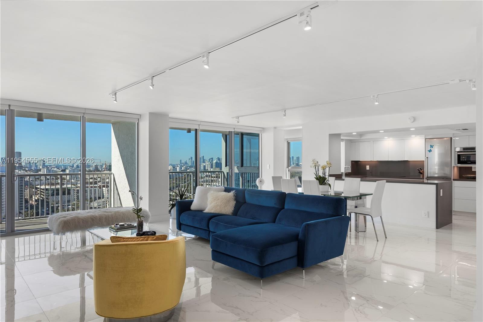 A modern living room features a blue sectional sofa, a yellow chair, and city views — 2655 Collins Ave, Miami Beach FL 33140, MIAMI BEACH, FL