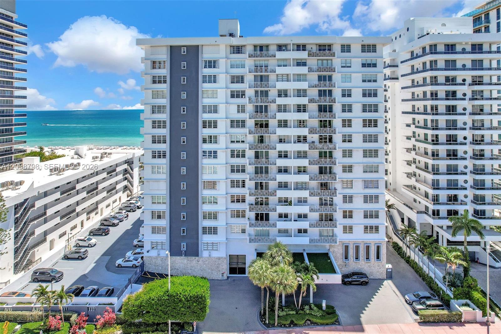 An exterior view of a multi-story white apartment building located near the ocean — 5825 Collins Ave # 2E, Miami Beach FL 33140, MIAMI BEACH, FL