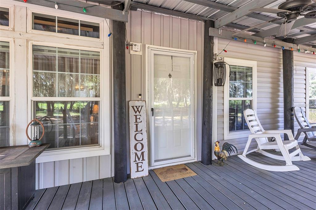 A covered porch features a white front door, rocking chairs, and a vertical welcome sign — 601 PURVIS ROAD, SEVILLE, FL