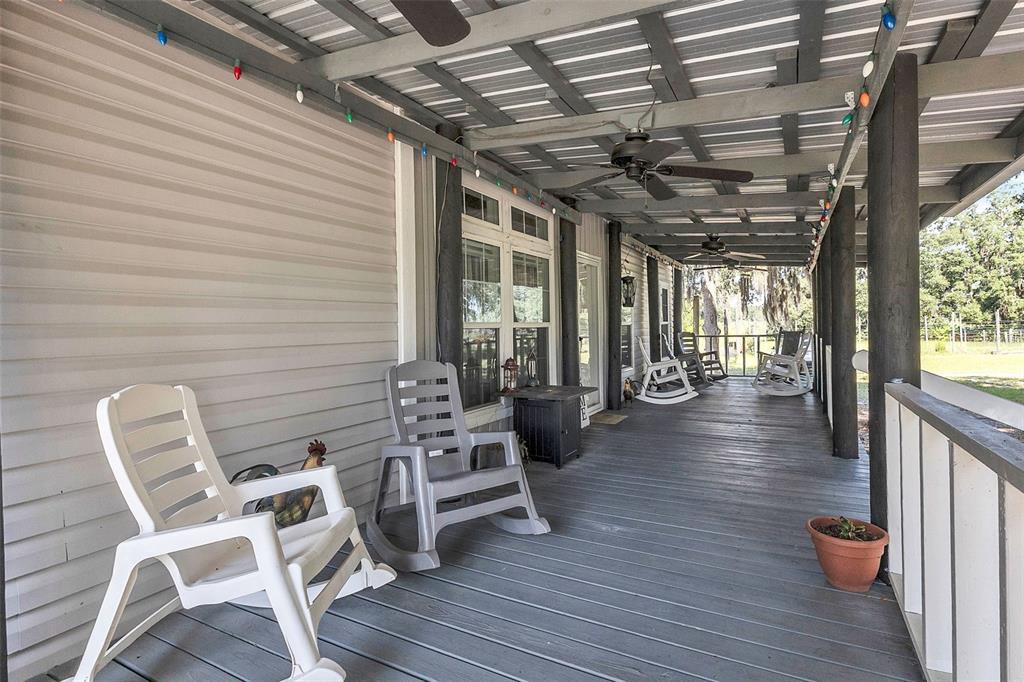 A covered wooden porch features several rocking chairs, ceiling fans, and string lights — 601 PURVIS ROAD, SEVILLE, FL