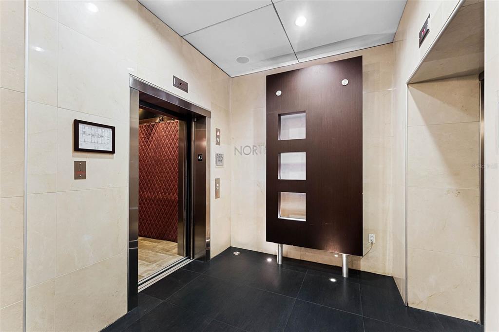An elevator lobby features beige tiled walls, dark floor tiles, and a modern decorative panel — 101 S EOLA DRIVE UNIT 815, ORLANDO, FL