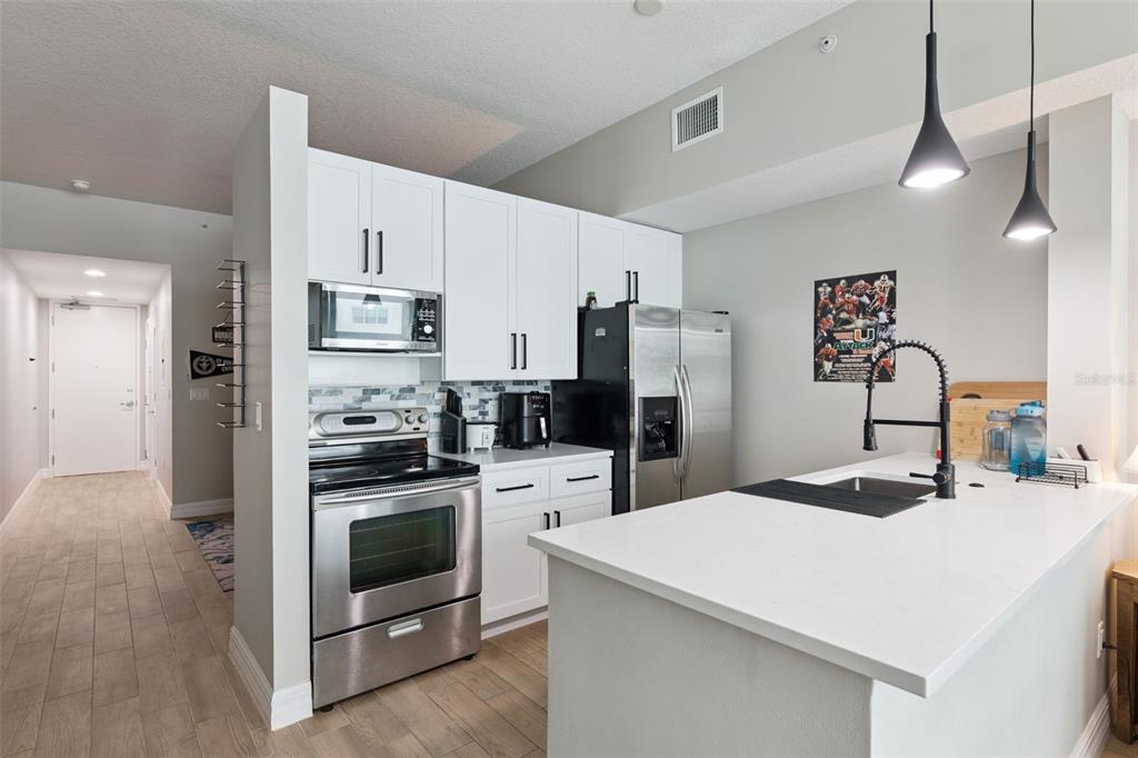 A modern kitchen features white cabinets, stainless steel appliances, and a white quartz island countertop — 101 S EOLA DRIVE UNIT 815, ORLANDO, FL