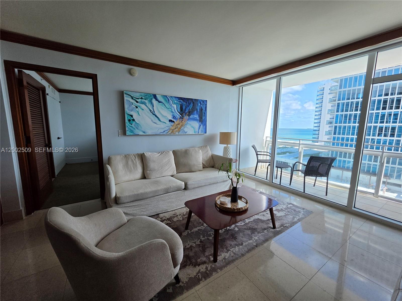 A living room features a beige sofa, an armchair, a coffee table, and a balcony view — 6801 Collins Ave, Miami Beach FL 33141, MIAMI BEACH, FL