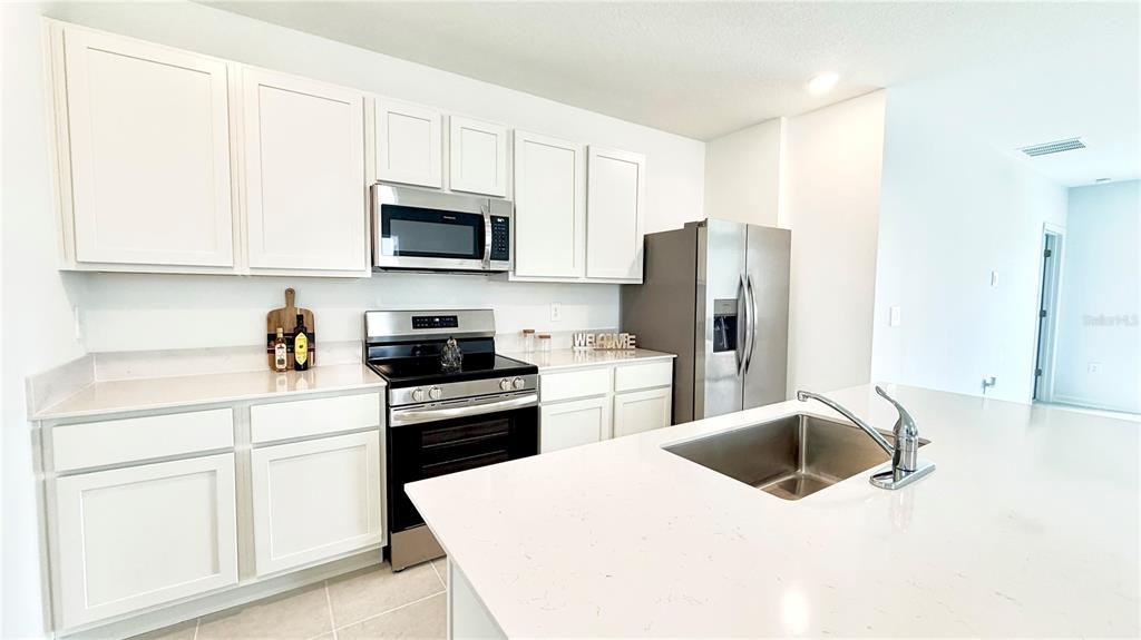 A kitchen features white cabinets, stainless steel appliances, and a large quartz-topped island — 4034 OLD MILL ROAD, HAINES CITY, FL