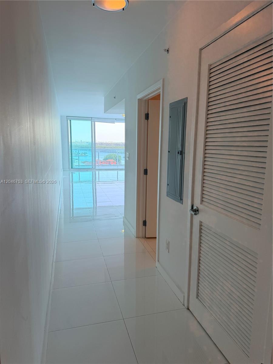 A hallway with white tile floors leads toward a balcony overlooking the water — SUNNY ISLES BEACH, FL