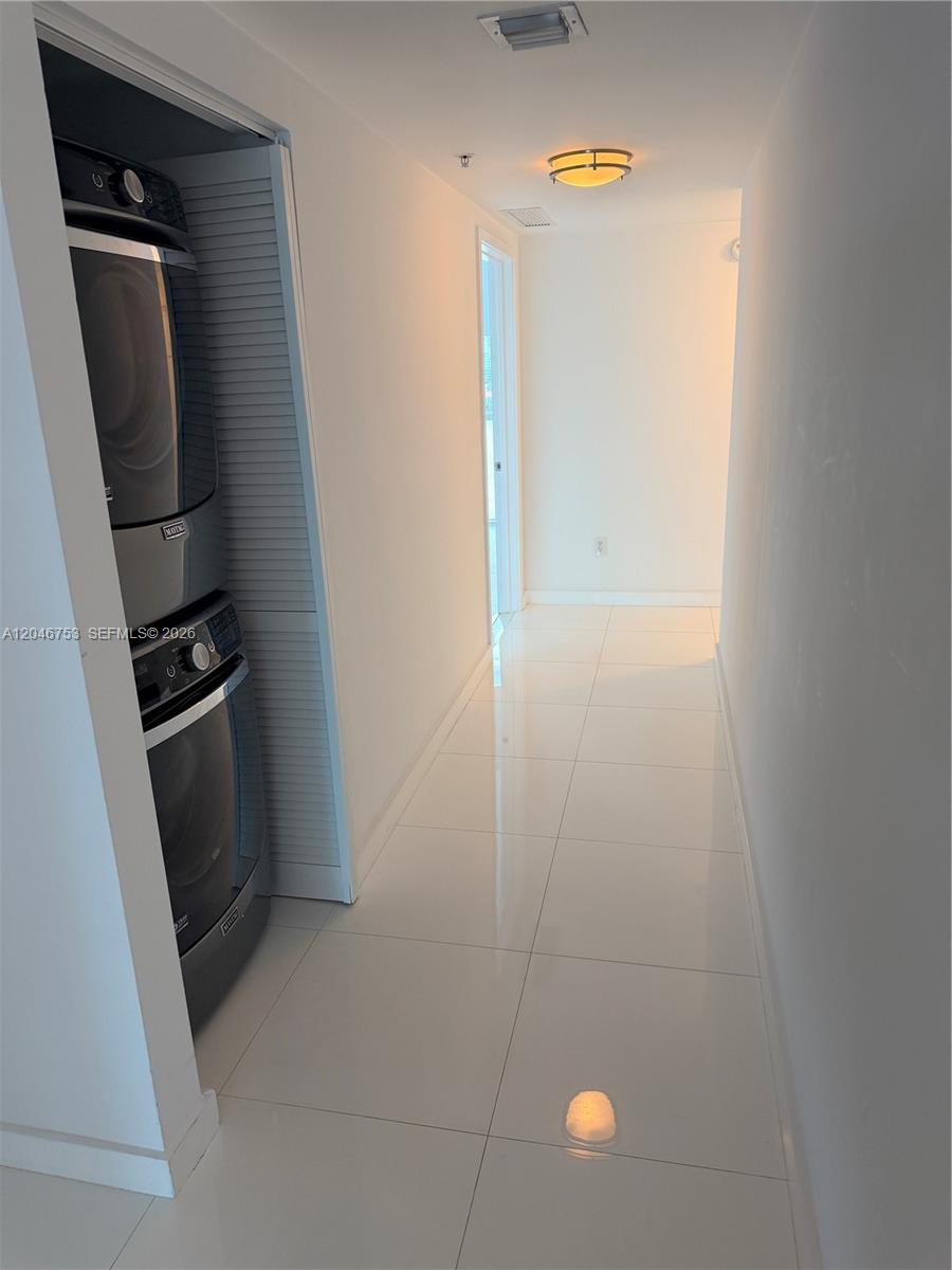A hallway features white tiled floors and a stacked washer and dryer unit — SUNNY ISLES BEACH, FL