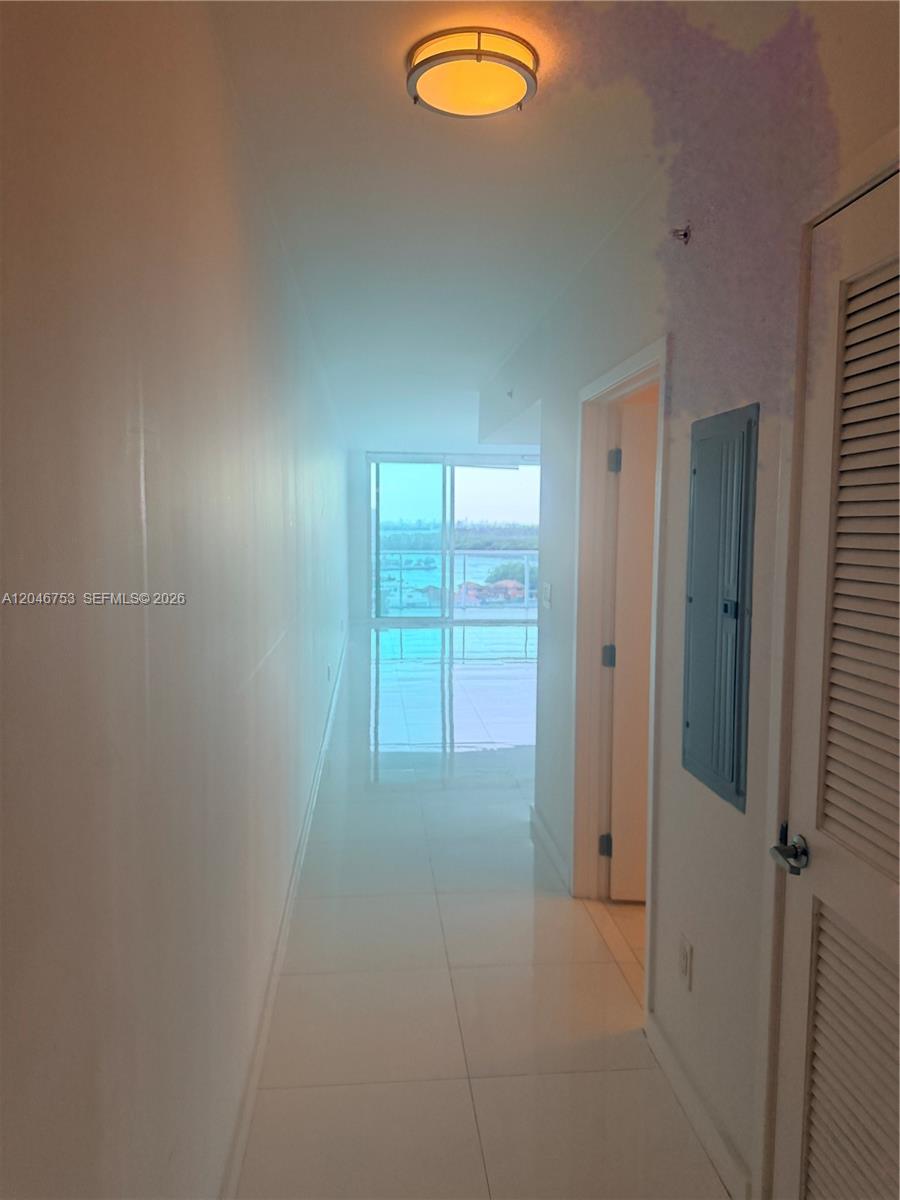 A hallway with white tile flooring leads toward a balcony with a water view — SUNNY ISLES BEACH, FL