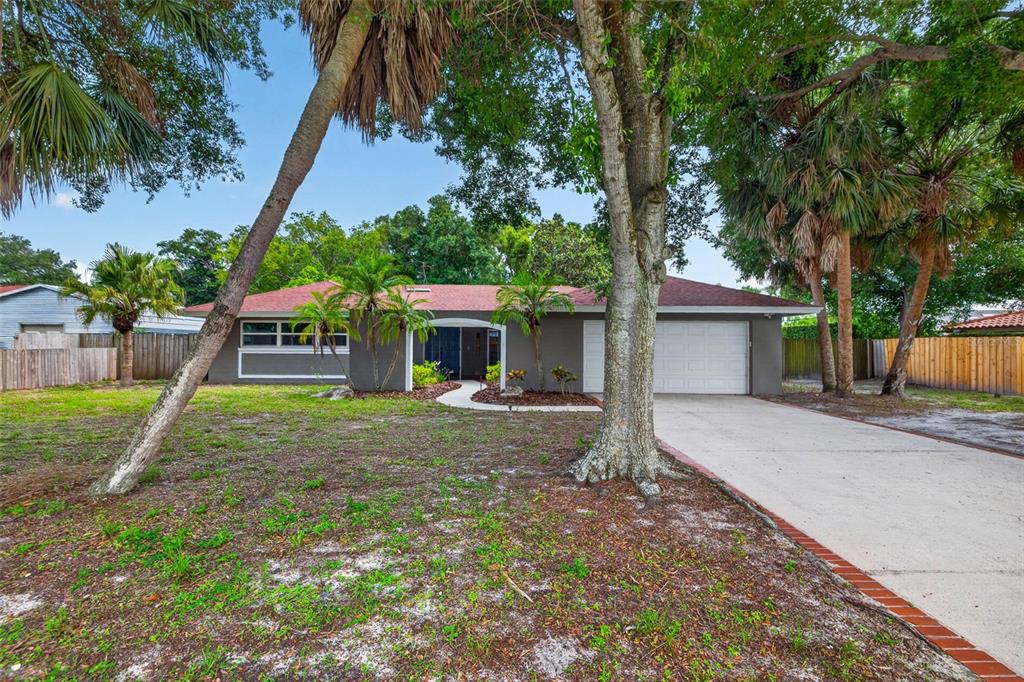 A single-story gray house with a red roof, white garage door, and surrounding palm trees — 1963 BELLEAIR ROAD, CLEARWATER, FL