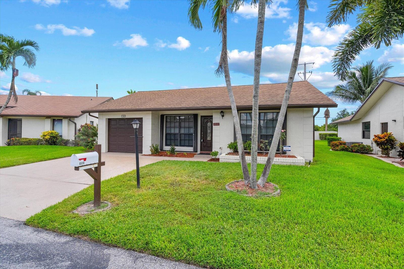 A single-story house with a brown roof, a garage, and palm trees in the front yard — 6510 Olivewood Circle, FL 33463, FL
