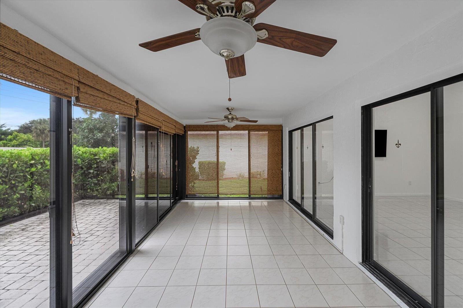 A sunroom with white tile floors, ceiling fans, and sliding glass doors overlooking a patio — 6510 Olivewood Circle, FL 33463, FL