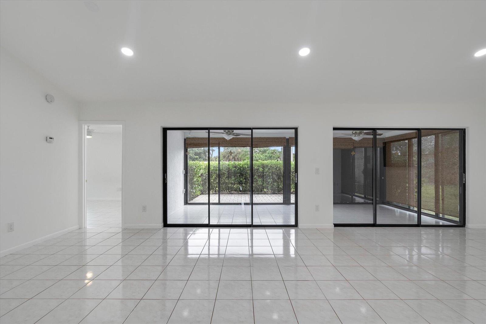 A bright, white-tiled living room features large sliding glass doors opening to a screened patio — 6510 Olivewood Circle, FL 33463, FL