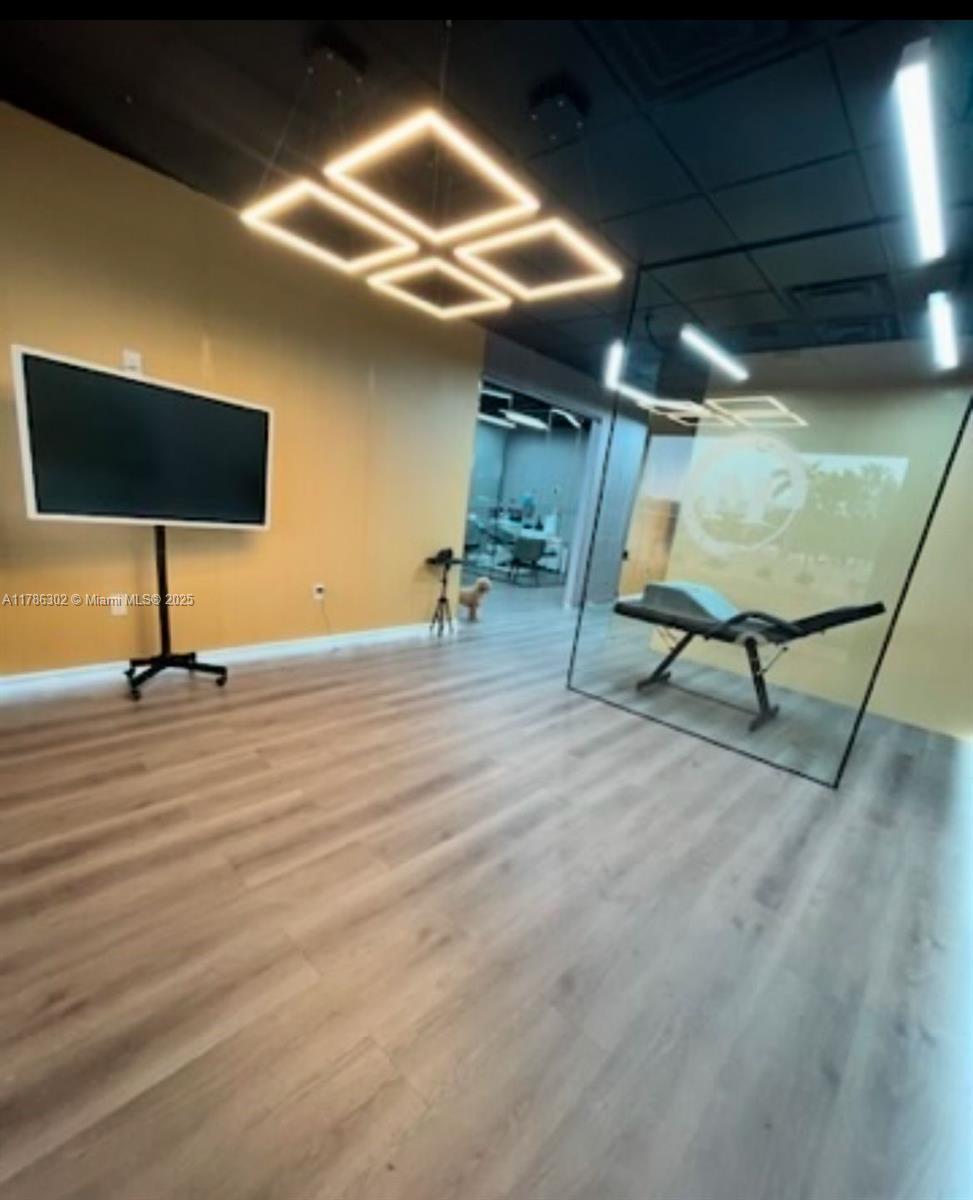 A modern room features light wood-look flooring, a wall-mounted television, and geometric LED light fixtures — Confidential, West Miami FL 33144, WEST MIAMI, FL