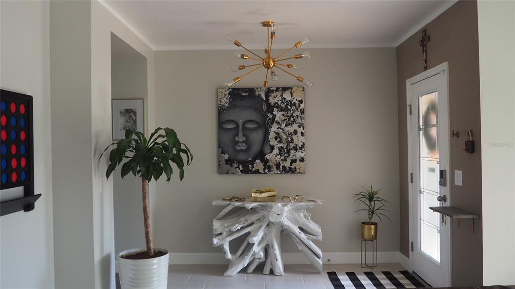 An entryway features a white driftwood console table, a Buddha wall art piece, and chandelier — 216 DENALI STREET, HAINES CITY, FL