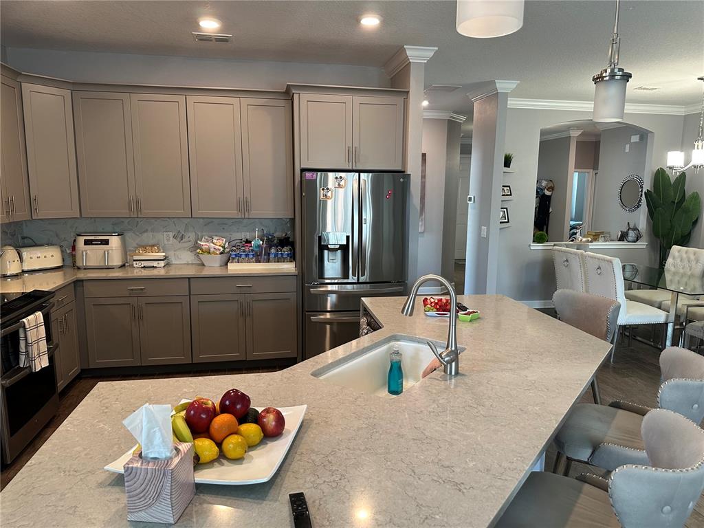 A kitchen features gray cabinets, stainless steel appliances, a large island with a sink, and seating — 1424 CLUBMAN DRIVE, DAVENPORT, FL