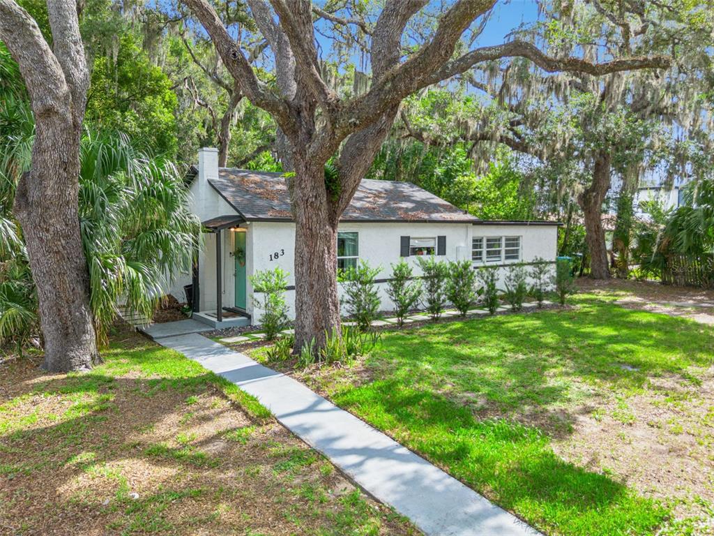 A small, white, single-story house with a front walkway sits under large, moss-covered oak trees — 183 E PINE AVENUE, LONGWOOD, FL
