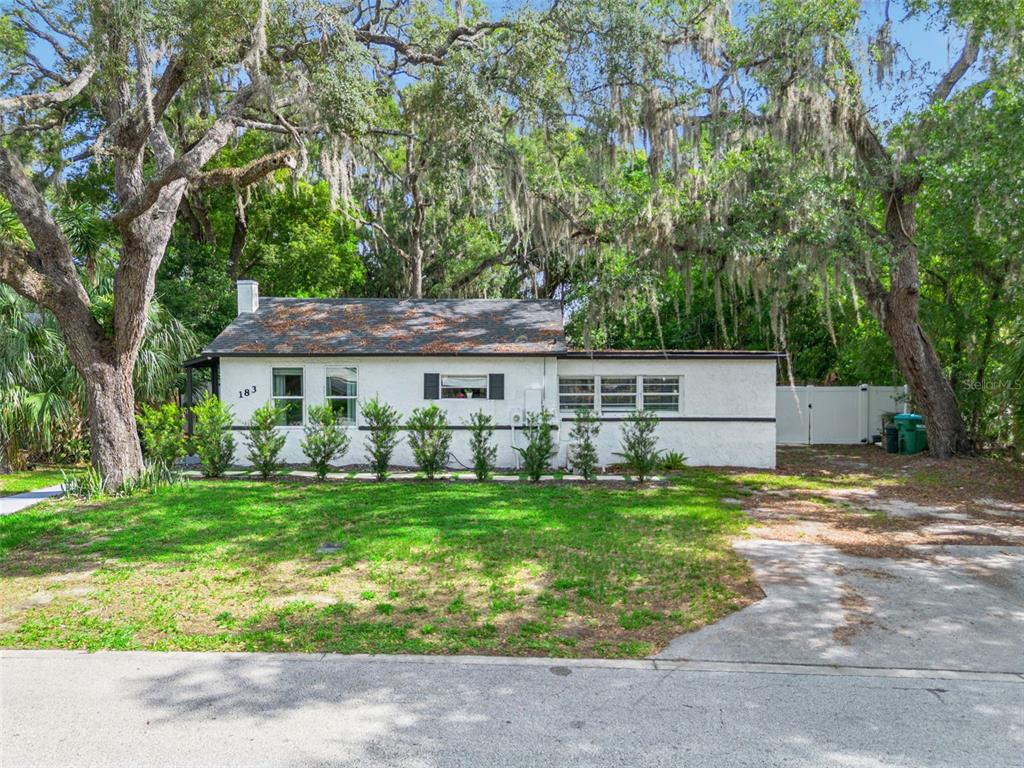 A single-story white house with a dark roof sits behind a lawn and large trees — 183 E PINE AVENUE, LONGWOOD, FL