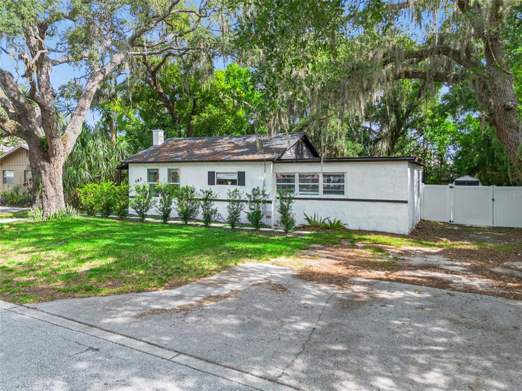 A white stucco house with a dark roof sits behind a lawn and concrete driveway — 183 E PINE AVENUE, LONGWOOD, FL