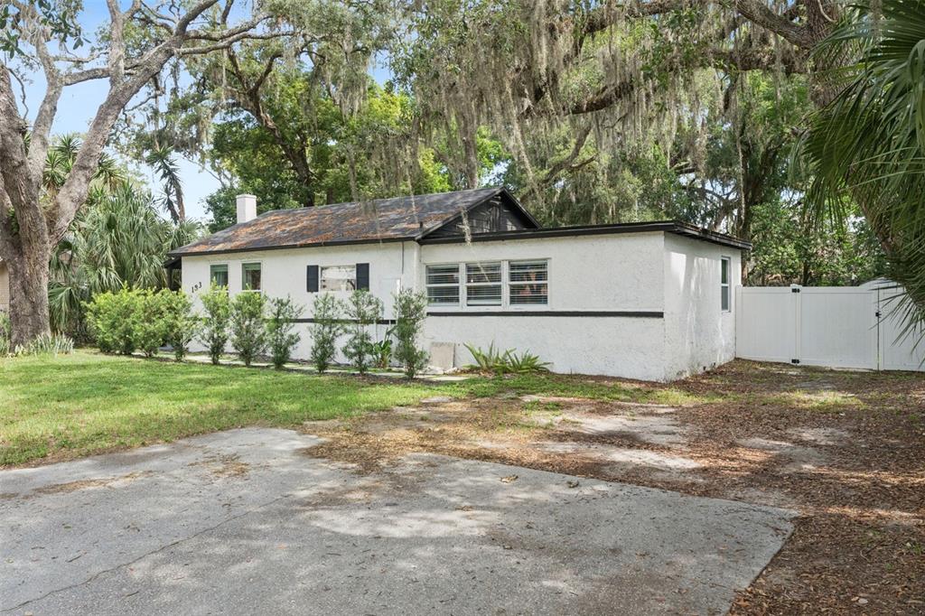 A white, single-story house with a dark roof sits on a lot with trees — 183 E PINE AVENUE, LONGWOOD, FL
