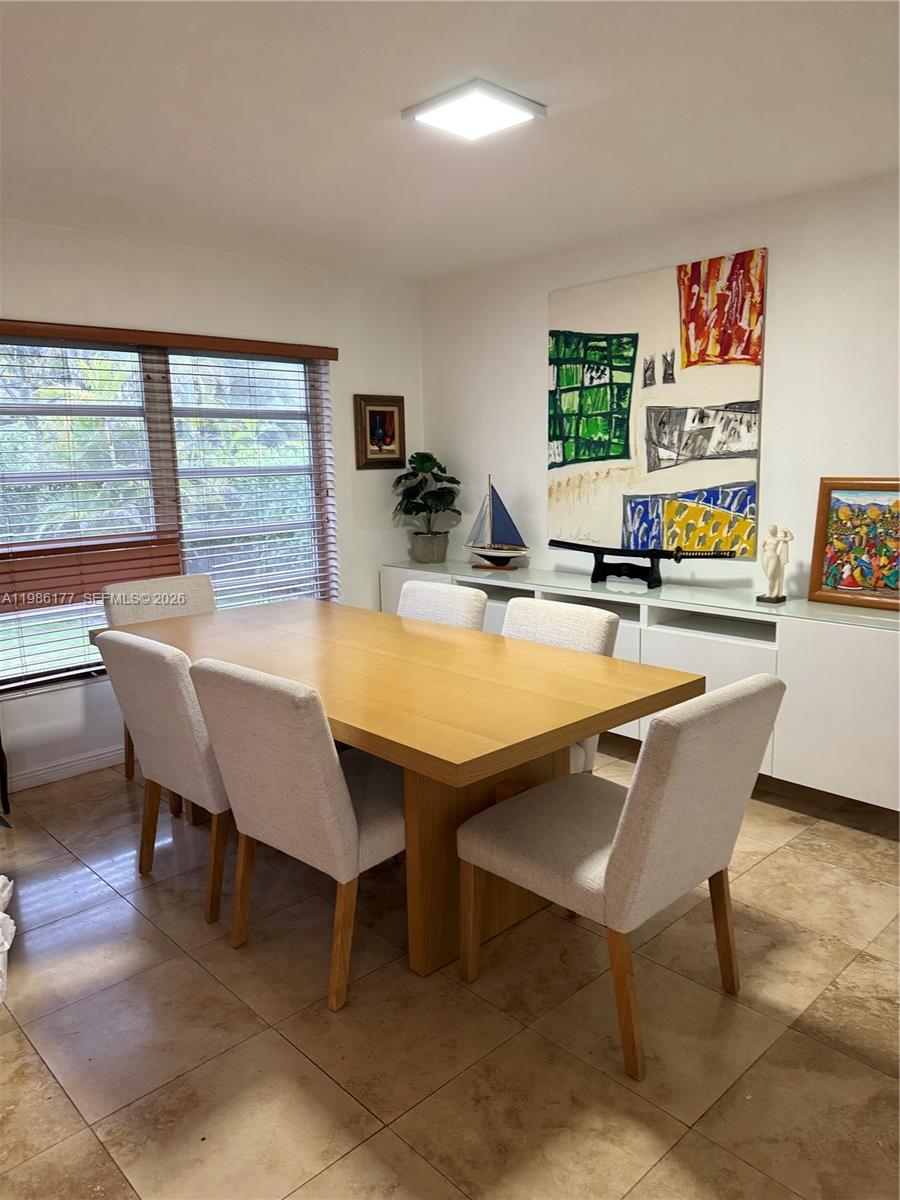 A dining room features a wooden table, light-colored chairs, tile flooring, and a large abstract painting — 1208 Bird Rd, Coral Gables FL 33146, CORAL GABLES, FL