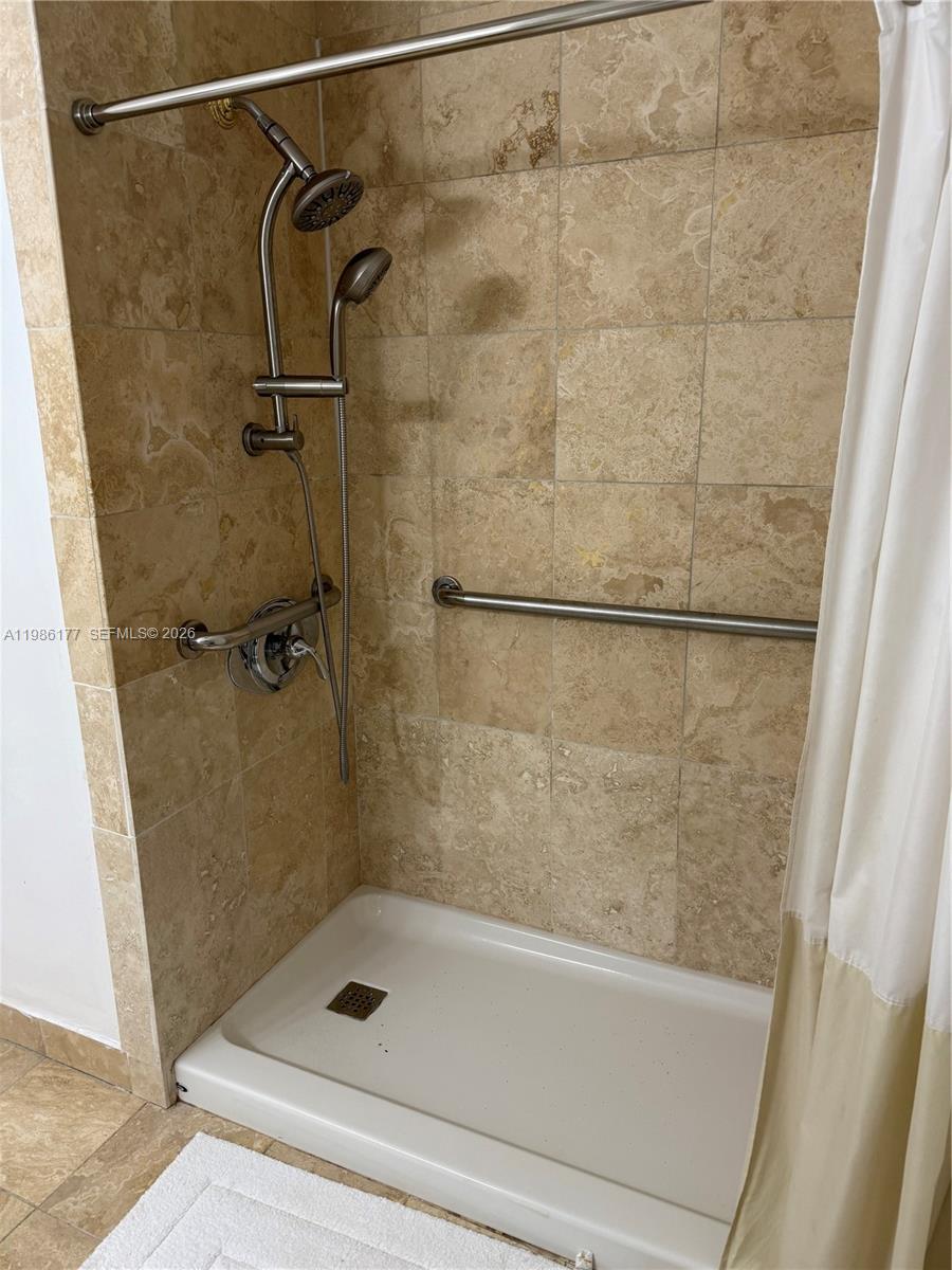 A walk-in shower features tan stone tile walls, a handheld showerhead, and a grab bar — 1208 Bird Rd, Coral Gables FL 33146, CORAL GABLES, FL