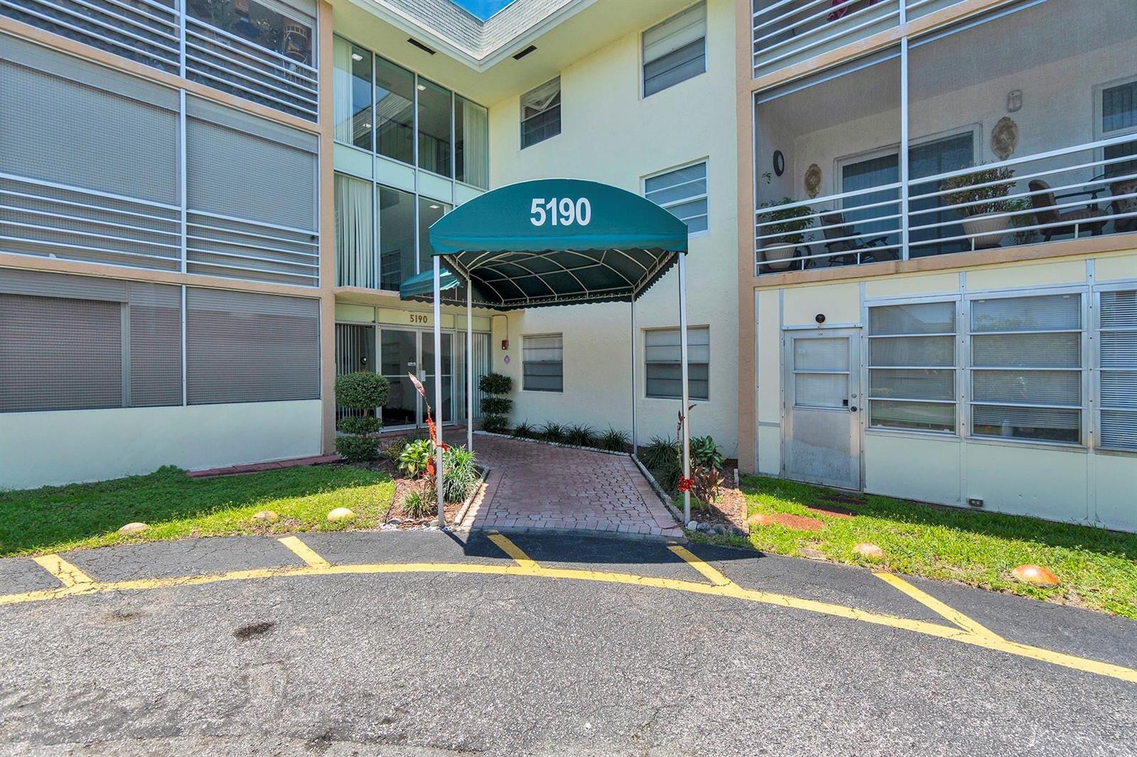 The exterior of a multi-story apartment building features a green awning over the entrance — 5190 E Sabal Palm Boulevard # 304, Tamarac FL 33319, TAMARAC, FL