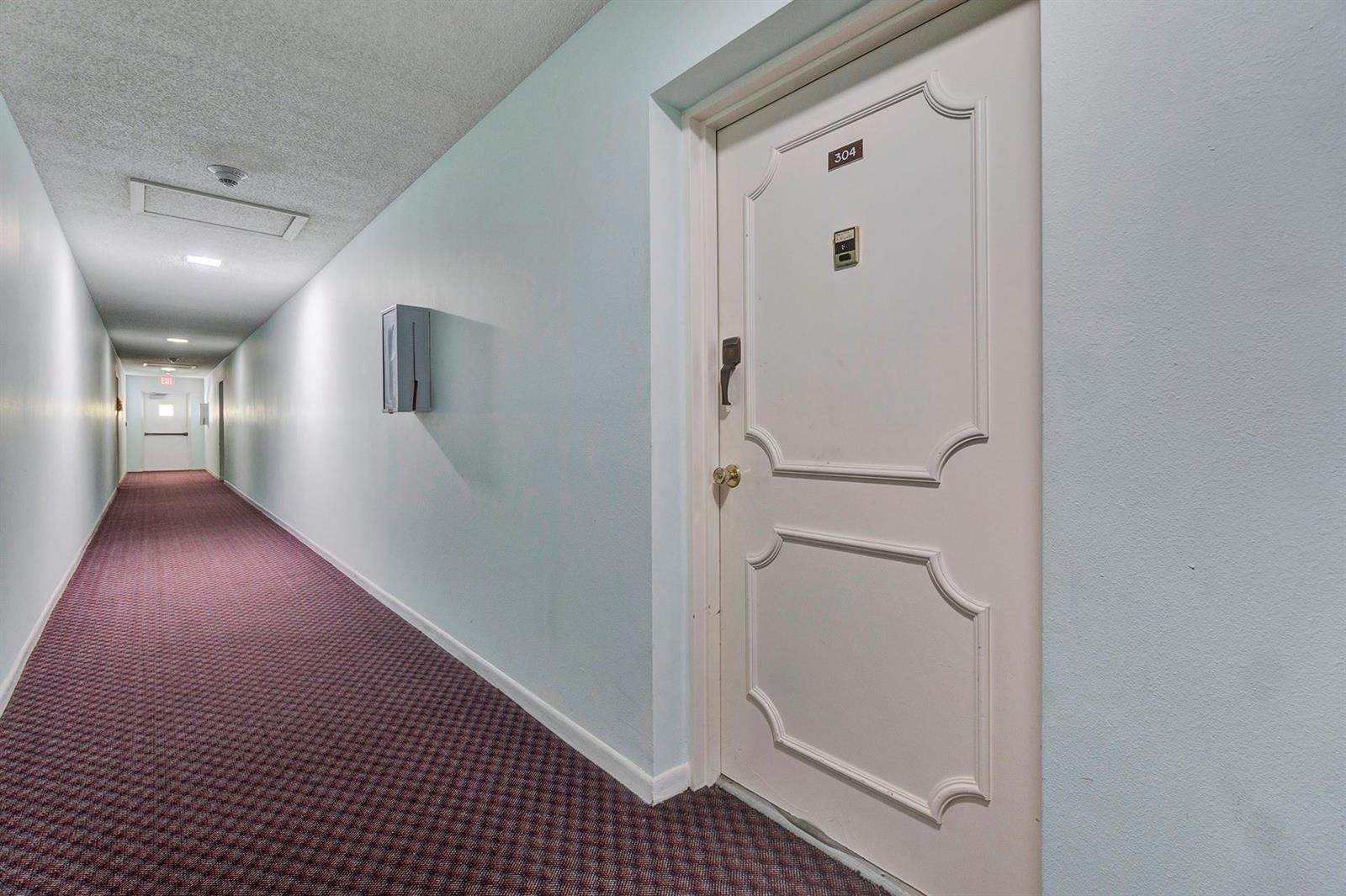 A long hallway with patterned carpet leads to a white door labeled 304 — 5190 E Sabal Palm Boulevard # 304, Tamarac FL 33319, TAMARAC, FL