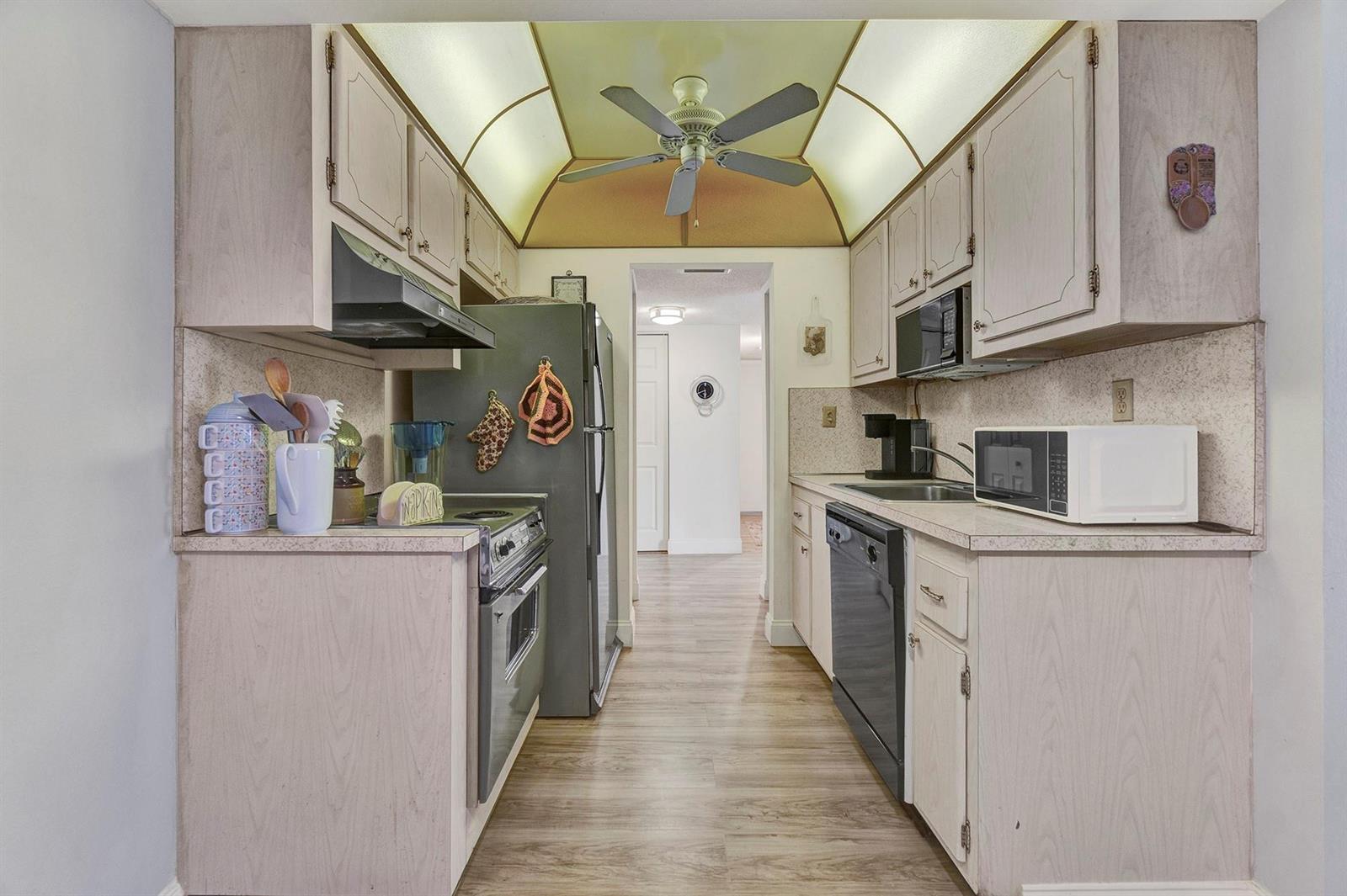 A galley kitchen features light wood cabinets, stainless steel appliances, and a vaulted ceiling fan — 5190 E Sabal Palm Boulevard # 304, Tamarac FL 33319, TAMARAC, FL
