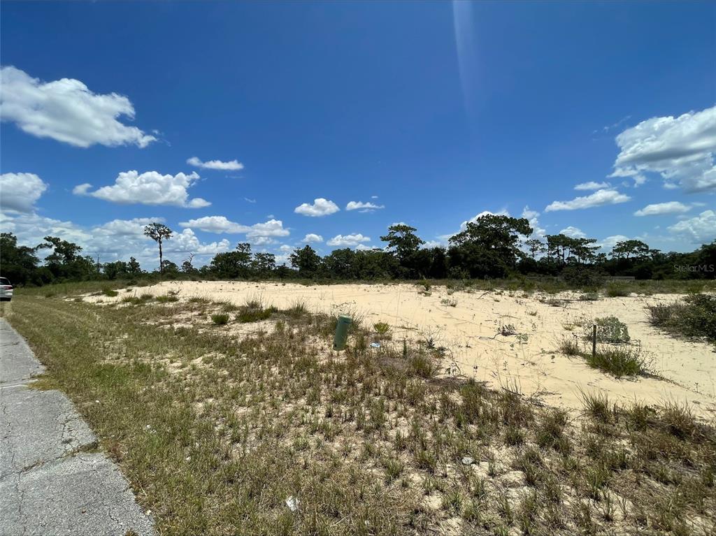 A vacant, sandy residential lot sits next to a paved road under a blue sky — 1344 HOMOSASSA COURT, POINCIANA, FL