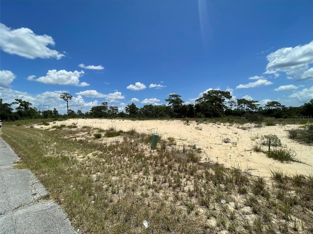 A vacant, sandy residential lot sits next to a paved road under a blue sky — 1344 HOMOSASSA COURT, POINCIANA, FL
