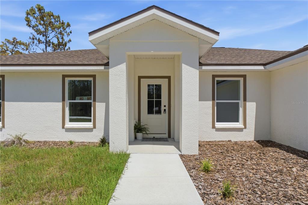 The exterior view shows a white stucco house with a covered entryway and brown trim — 14586 MOCKING WREN ROAD, WEEKI WACHEE, FL